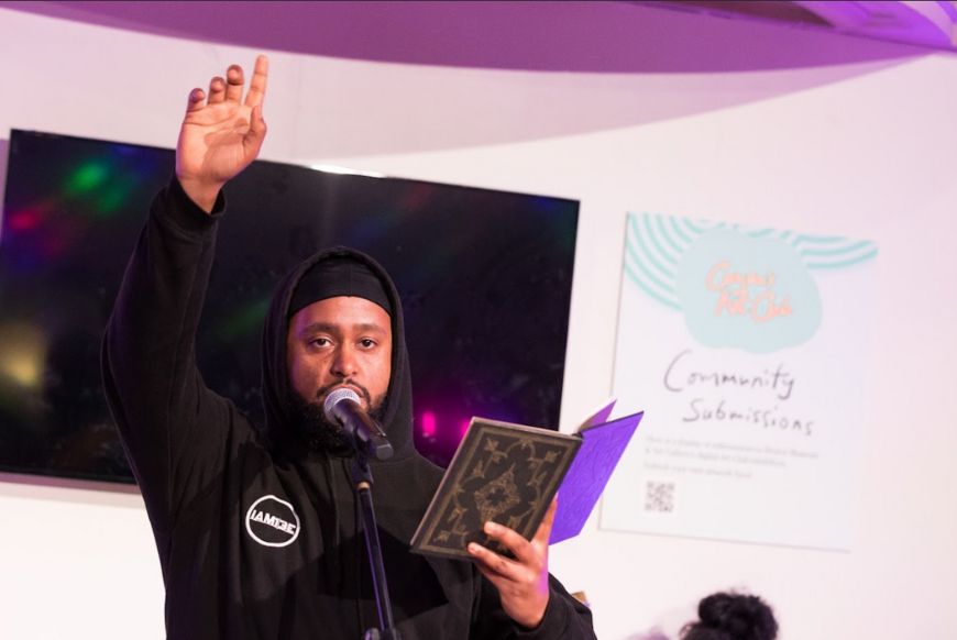 A man reading from a book into a microphone with his arm raised